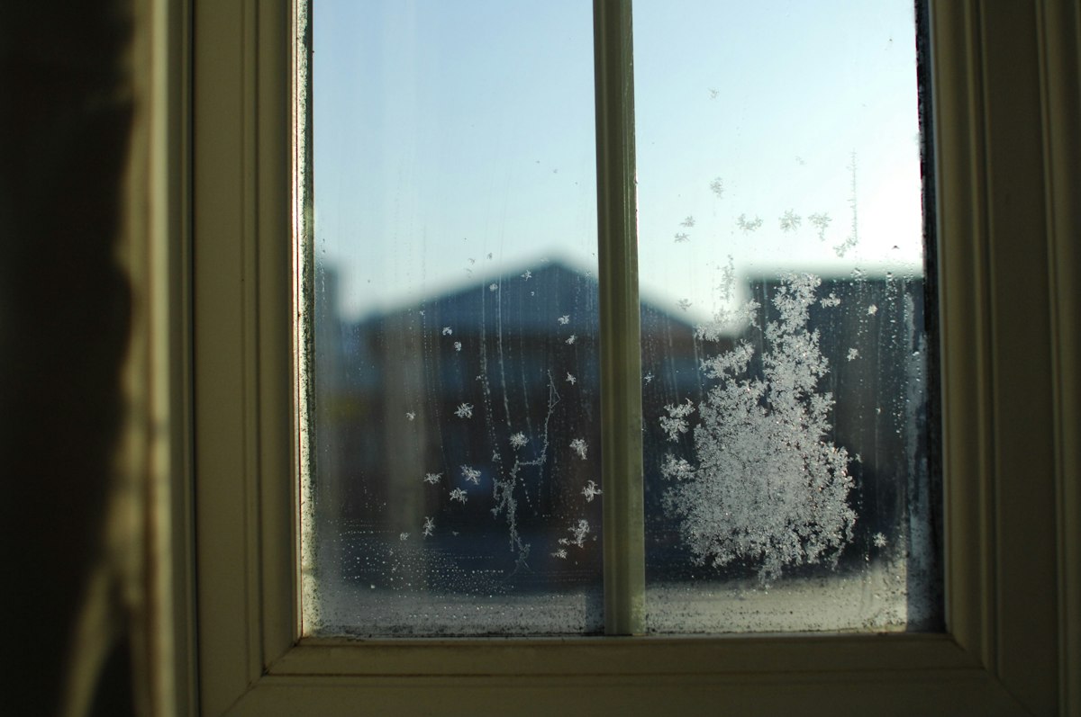 A wooden-framed window with frost and condensation on the glass