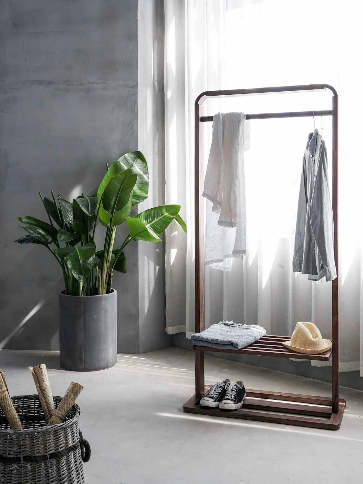 A wooden clothes rail with shirts drying by a window with white curtains