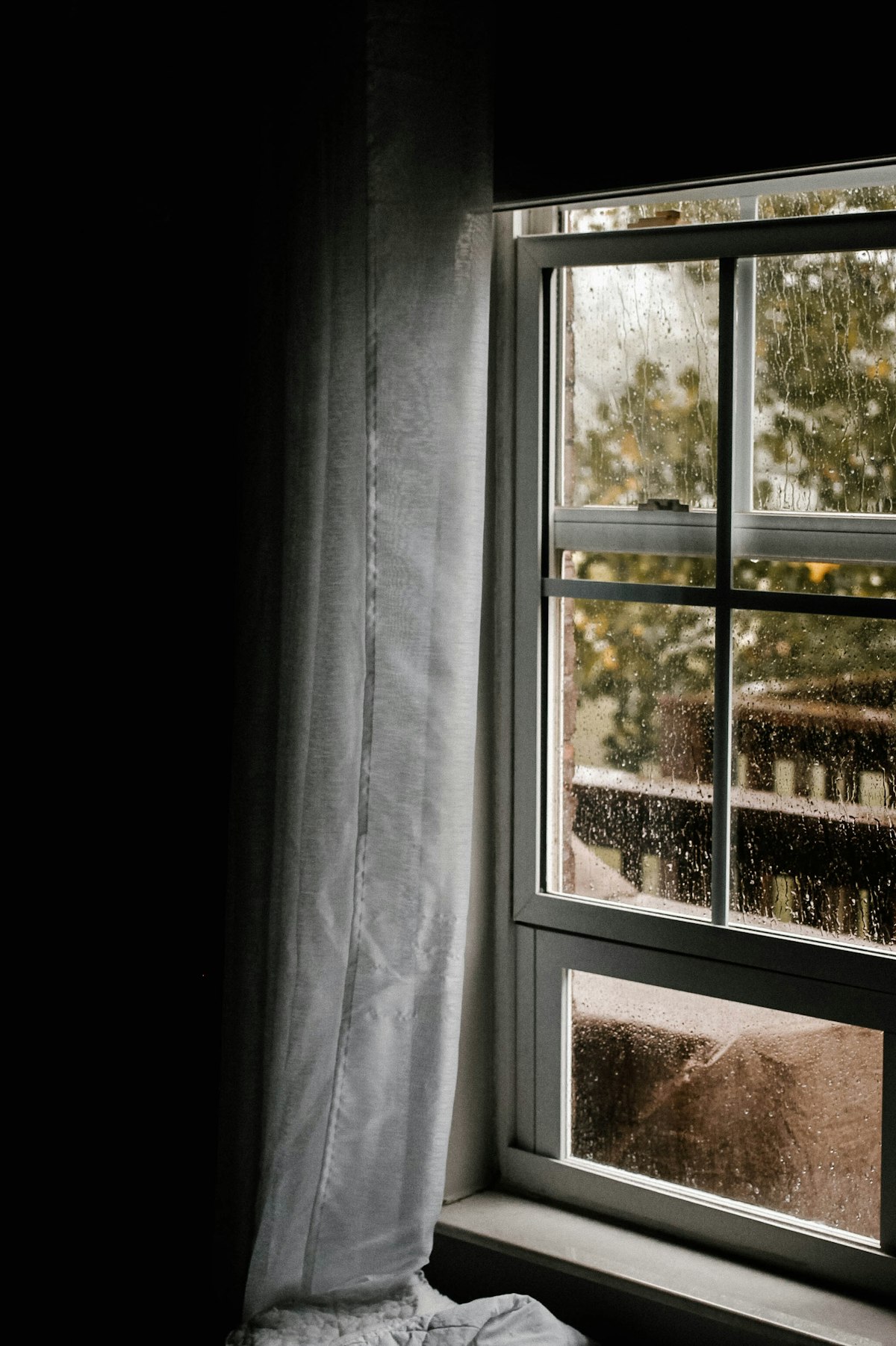 Water droplets on a sliding window behind a sheer curtain in a dim room