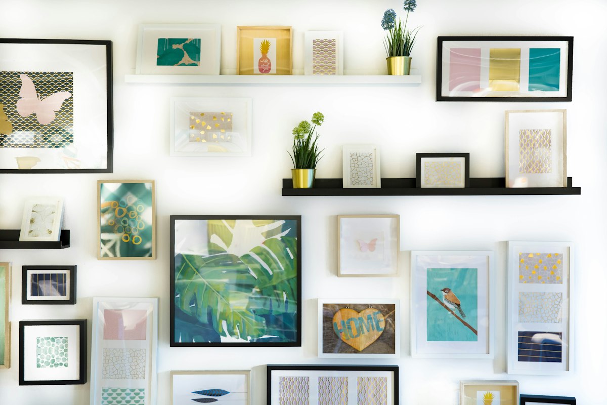 A white wall with colourful framed prints on narrow picture shelves