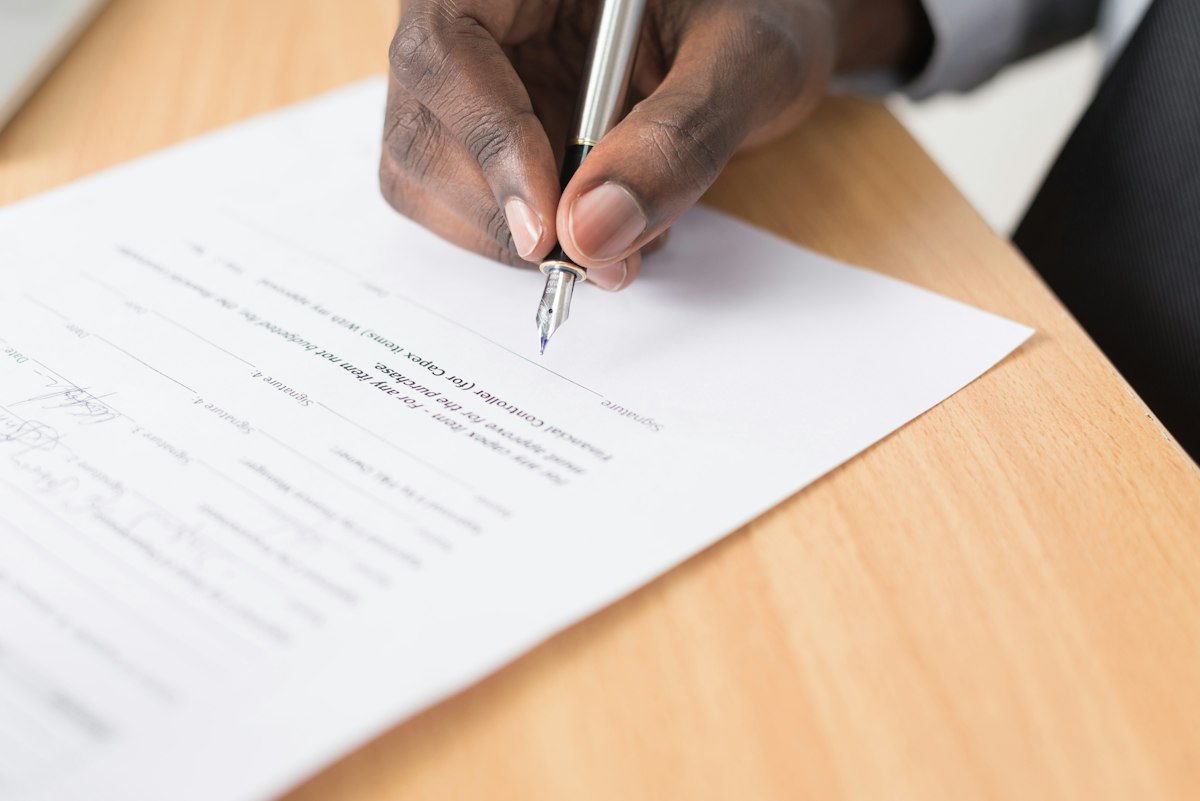 A person writing on a sheet of paper at a wooden desk
