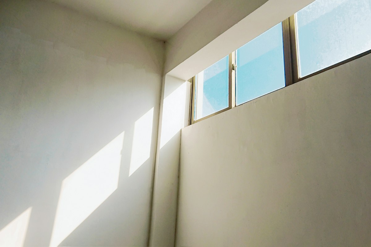A plain cream-painted wall lit by sunlight from high windows