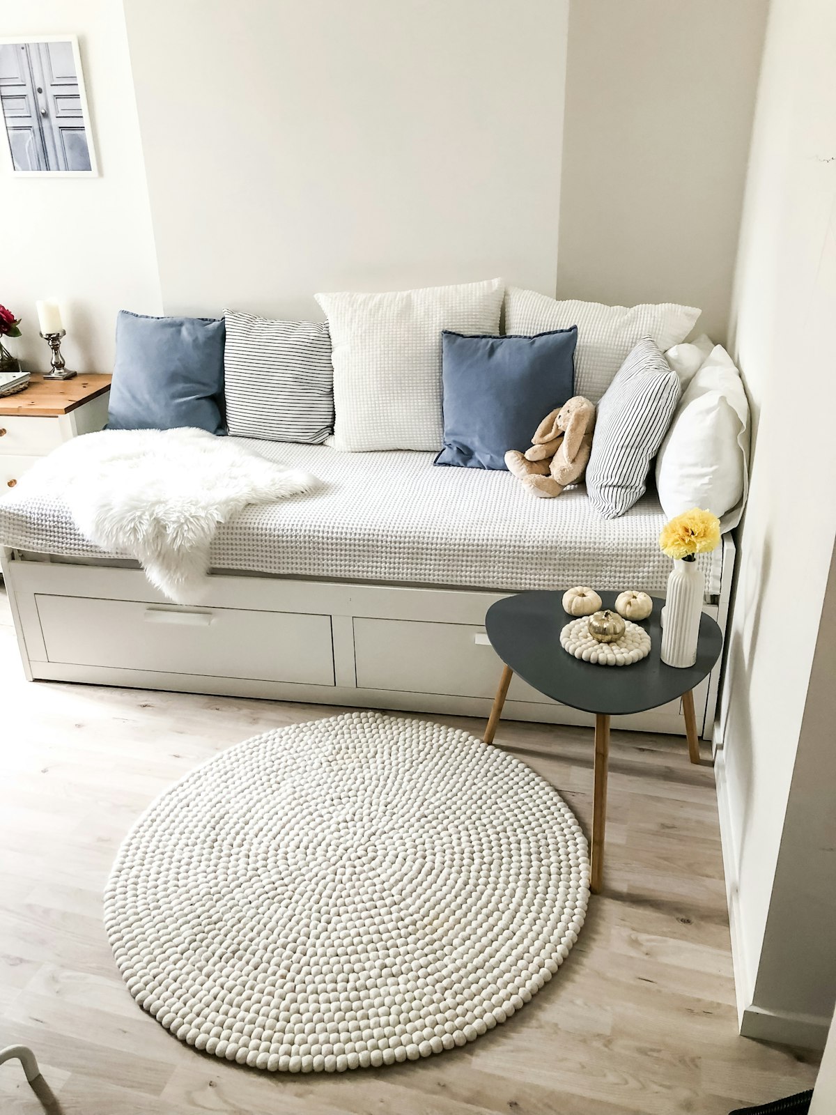 A white sofa bed with blue and white cushions and a round woven rug