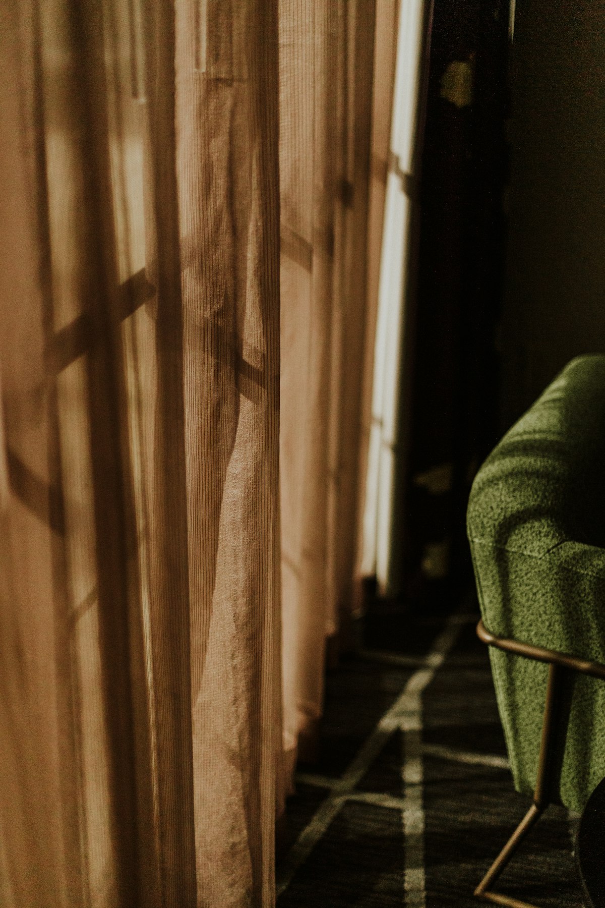 Long brown curtains with sunlight falling across a green armchair