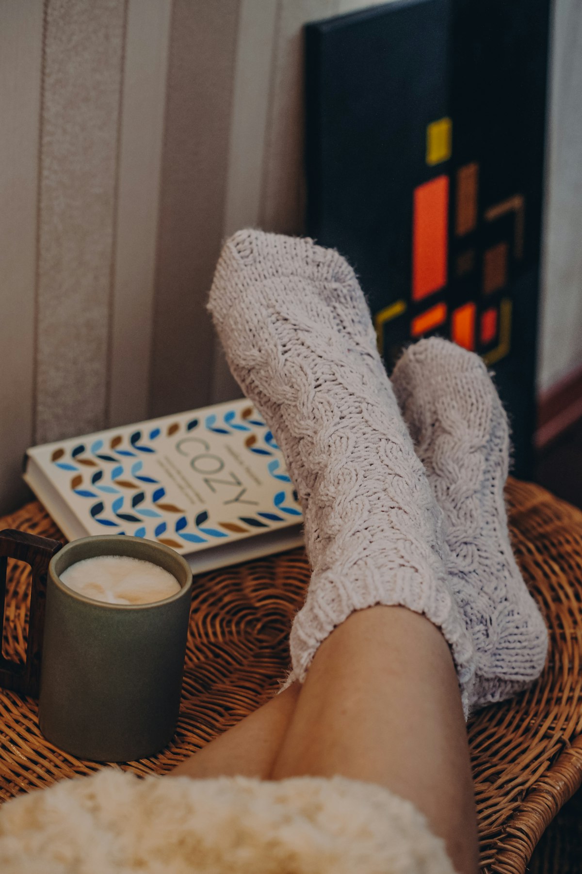 Feet in thick knitted socks next to a mug and a book