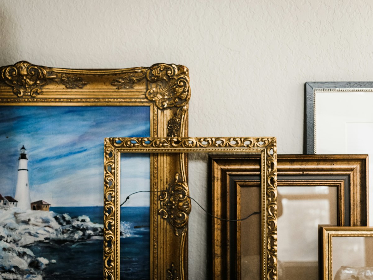 Ornate gold picture frames and paintings leaning against a white wall