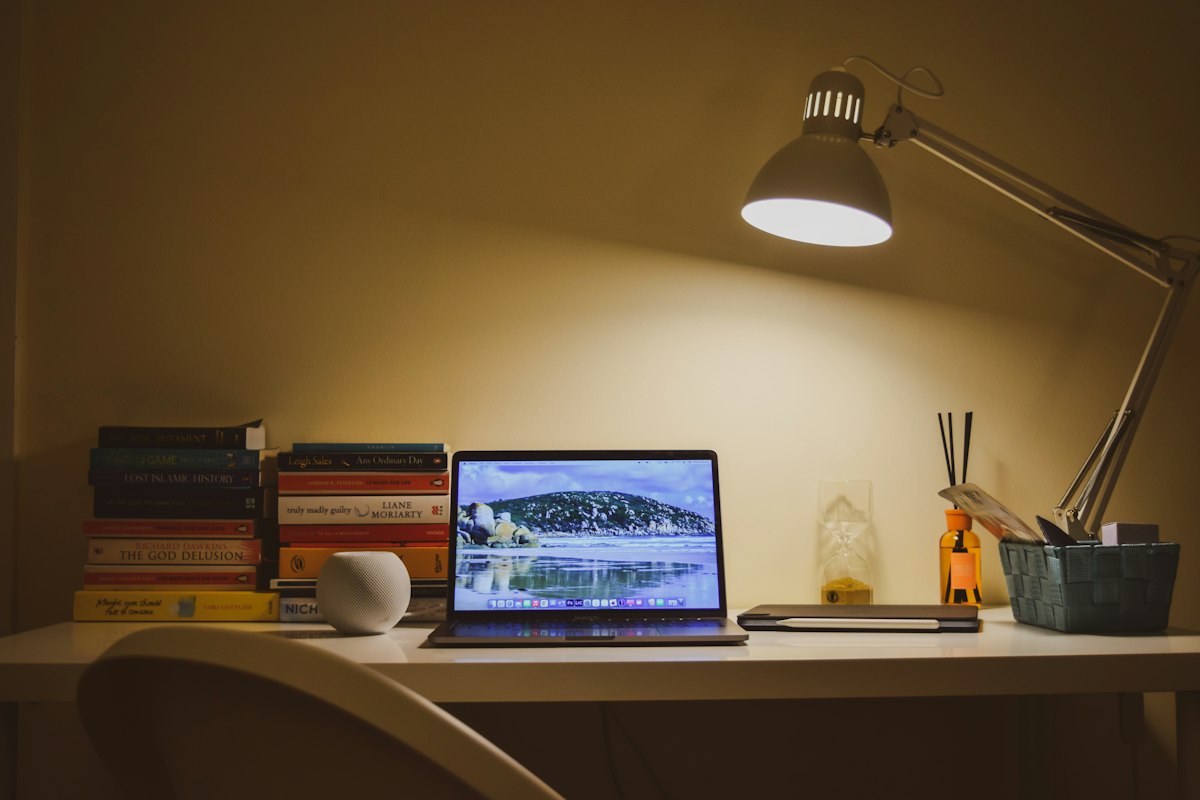 A laptop on a small desk lit by a lamp