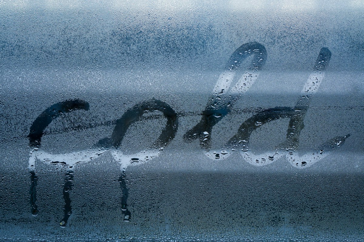 The word cold written with a finger in condensation on a misted window