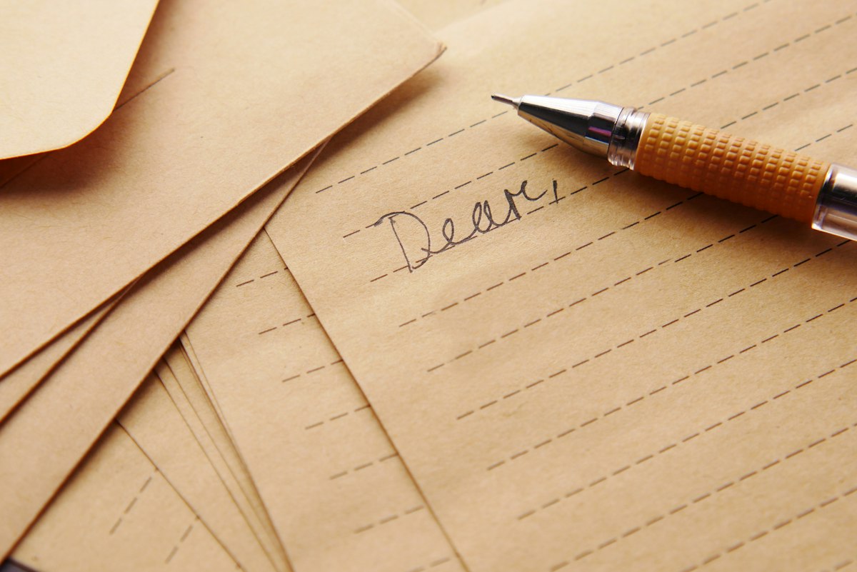 A pen resting on a handwritten letter beginning Dear