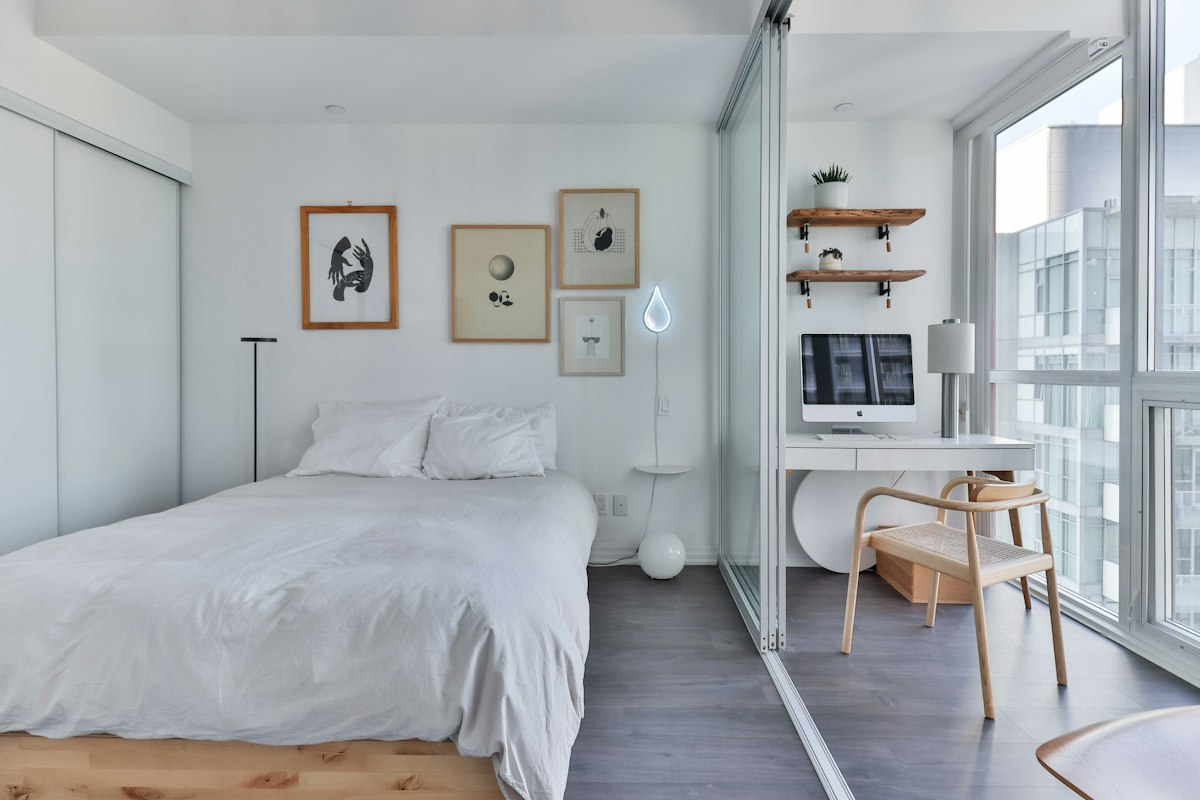 A bright white studio flat with a bed, a small desk and floor-to-ceiling windows