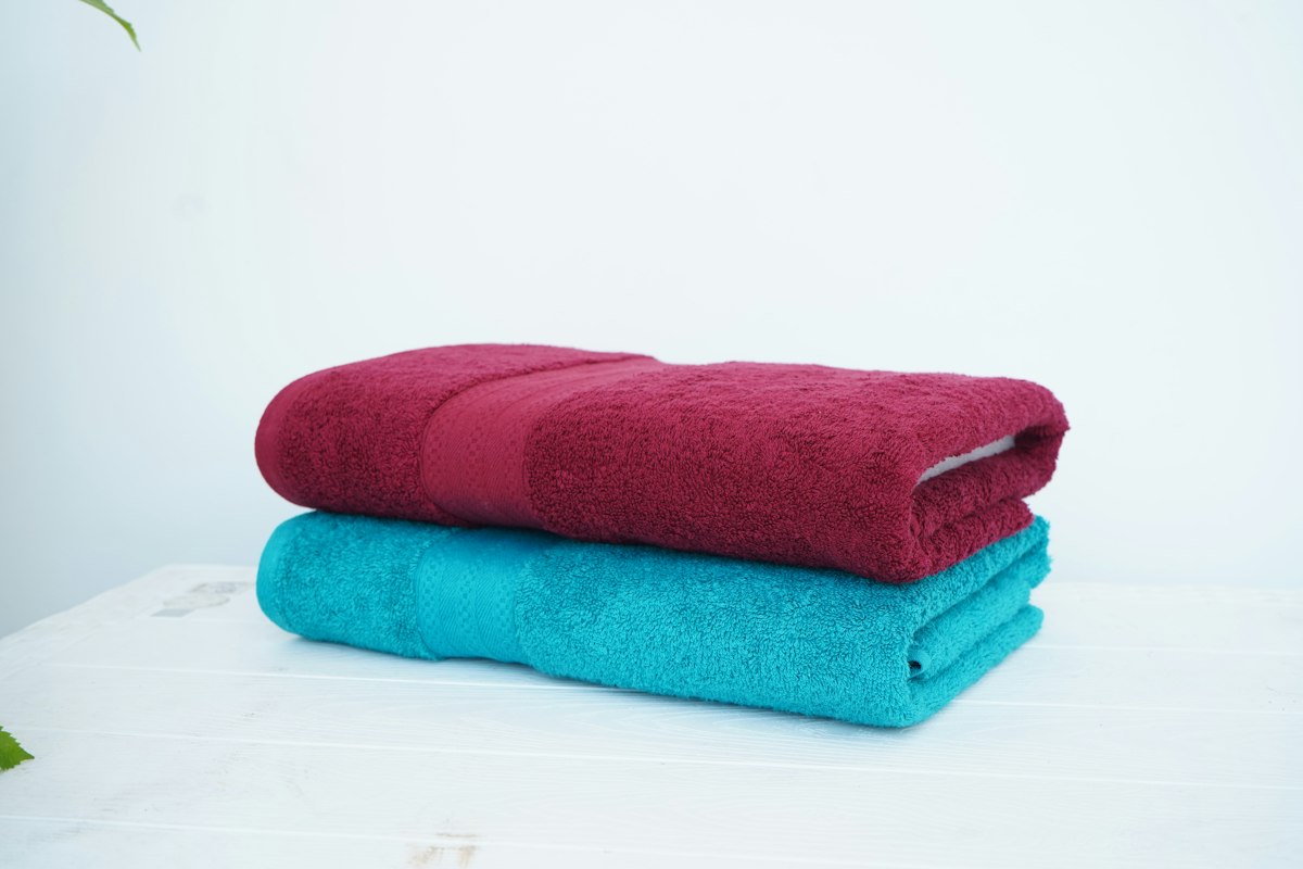 Two folded bath towels, one red and one turquoise, on a white surface