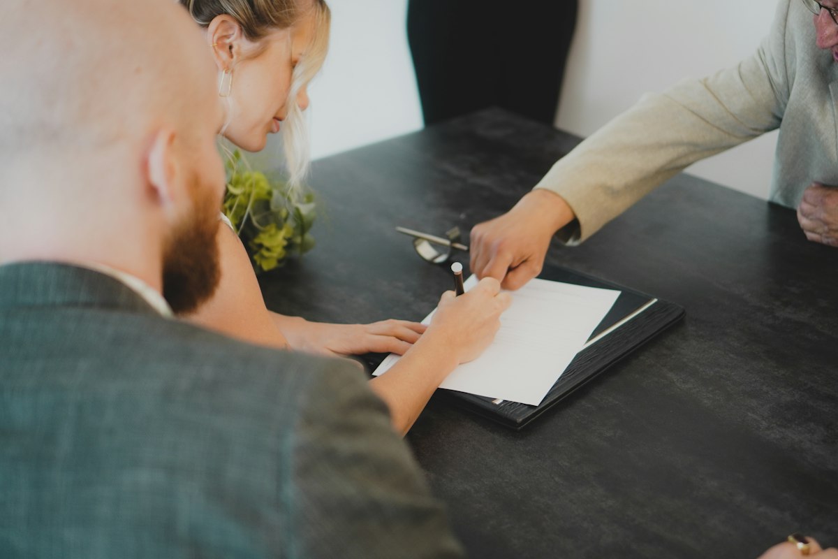 Two people at a desk signing a document with a pen