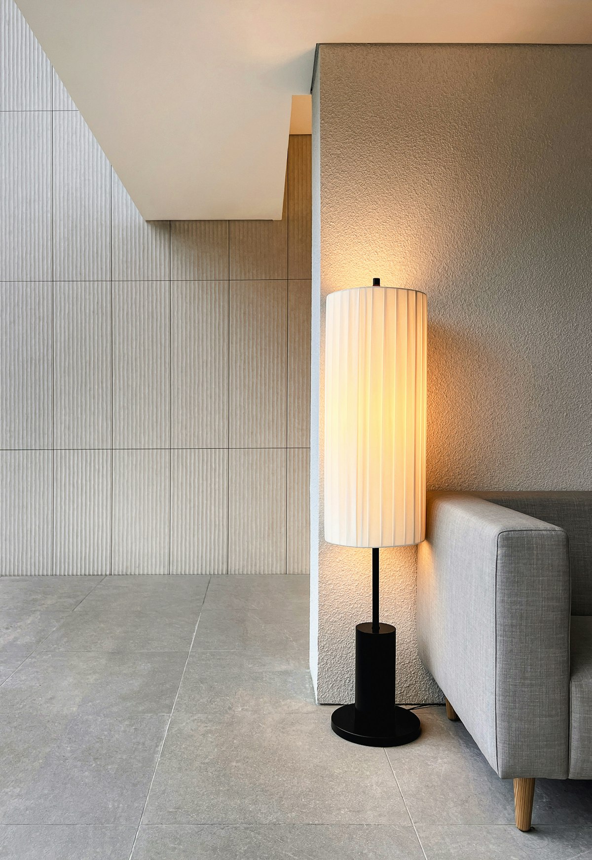 A tall floor lamp with a paper shade beside a grey sofa in a pale room