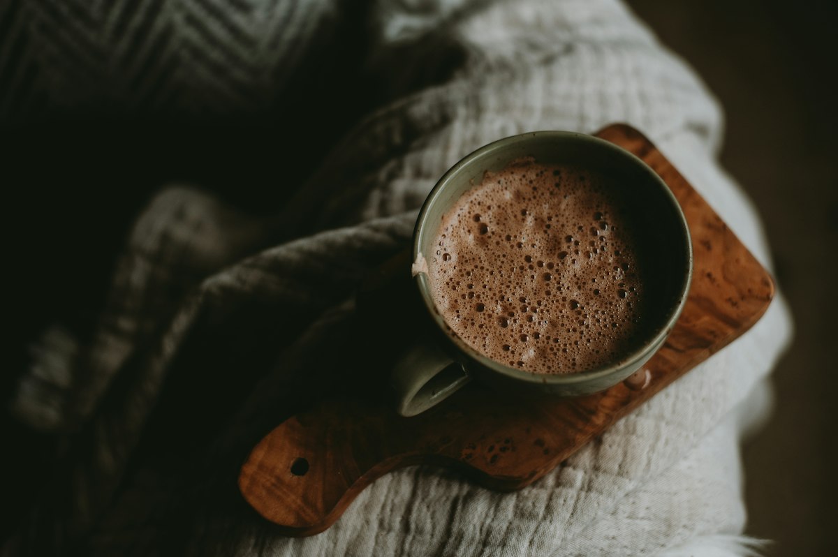 Hands in a knitted jumper holding a mug of hot chocolate on a wooden board