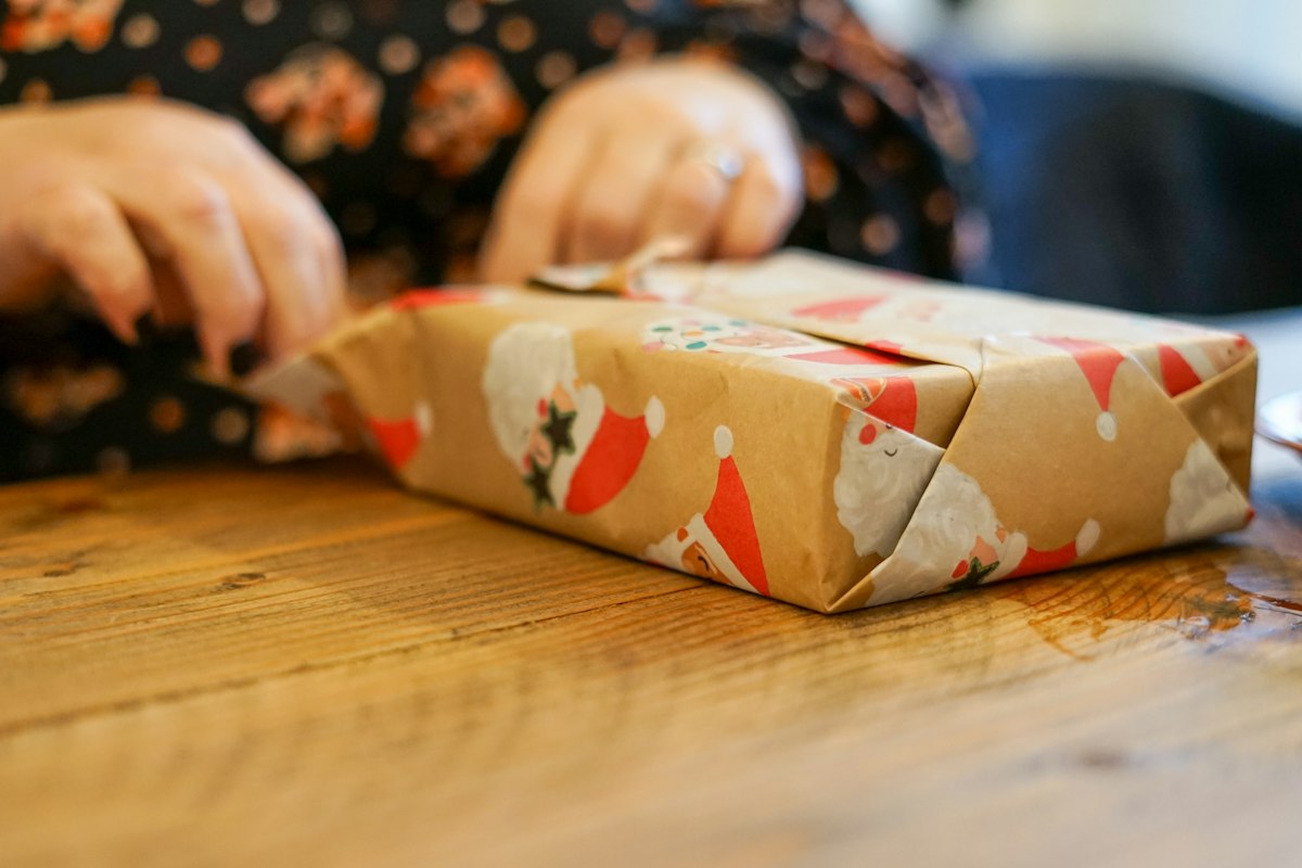 A person wrapping a small present in patterned paper on a wooden table