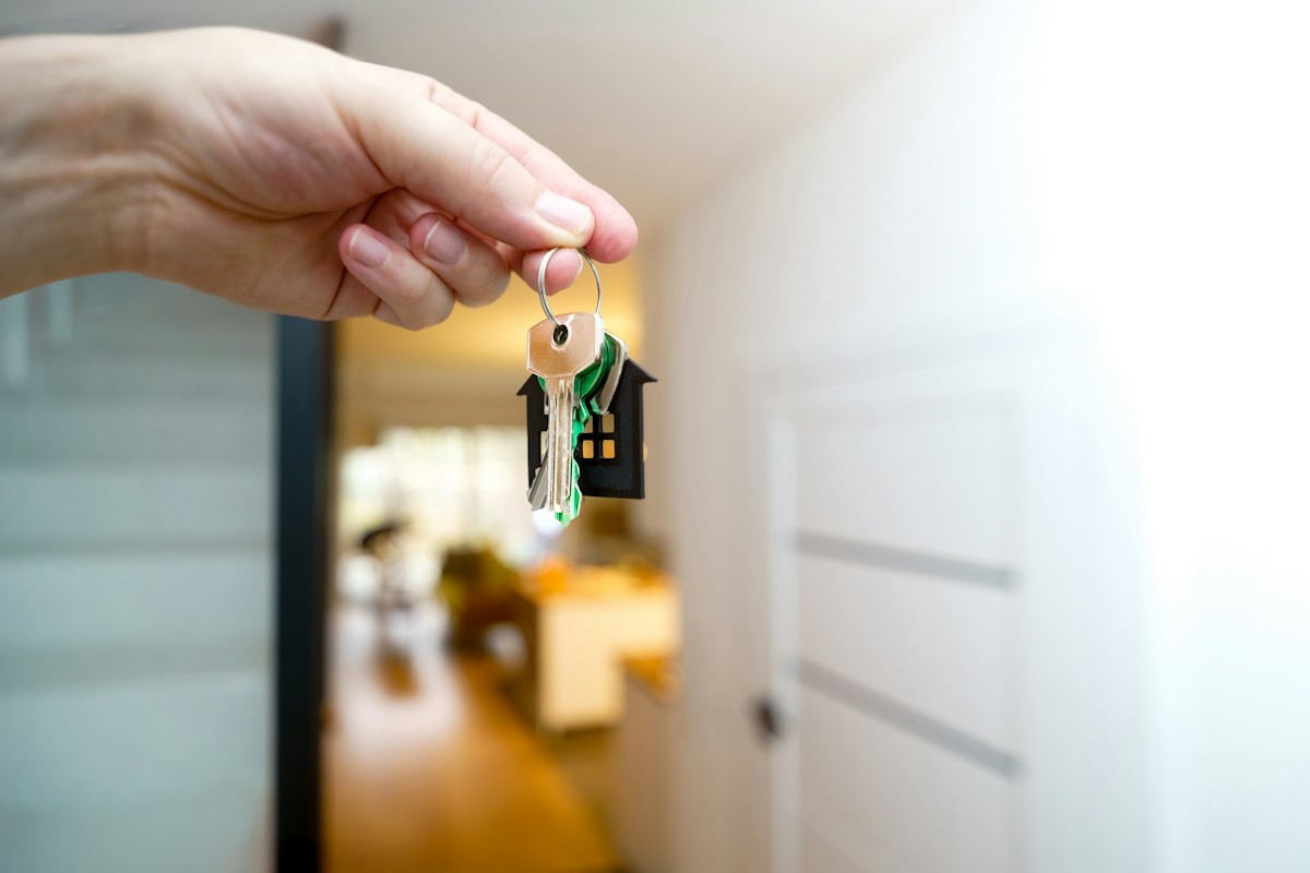 A hand holding a set of house keys in front of an open front door