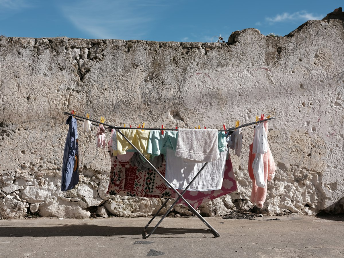 Clothes and towels drying on a folding rack against a rough wall