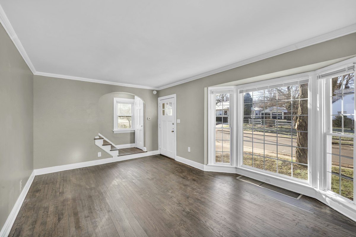 An empty living room with grey walls, wood-effect floor and a bay window